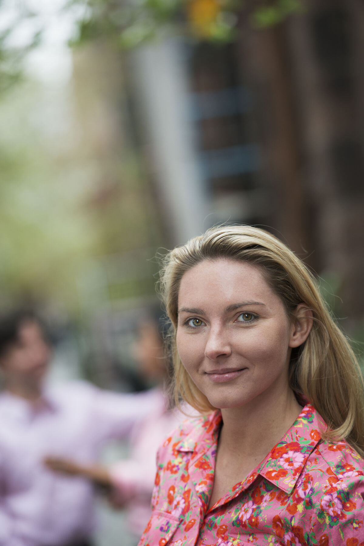 A woman with long blonde hair walking on a city street in soft spring light.