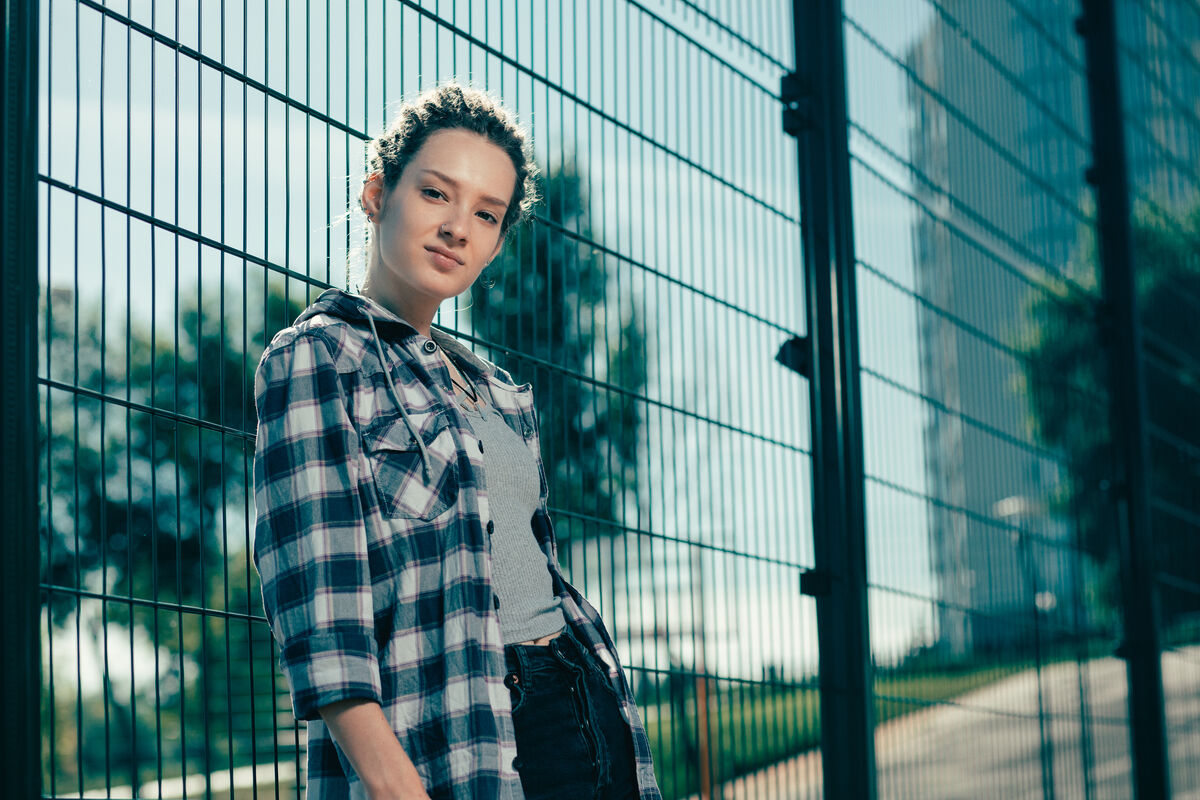 A young woman in casual clothes sitting calmly outdoors, looking thoughtful.